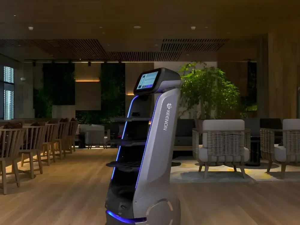 Robot serveur Keenon à plateaux circulant dans une salle, fauteuils et plantes en arrière-plan