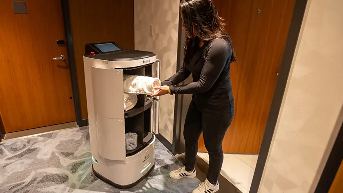 Robot de livraison remettant du linge à une employée dans un couloir d'hôtel
